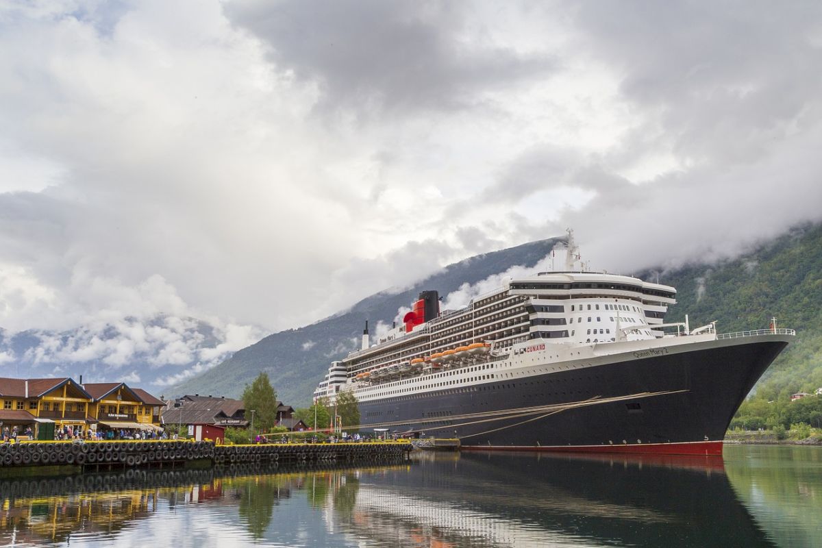 A large cruise ship is docked in a body of water with mountains in the background.