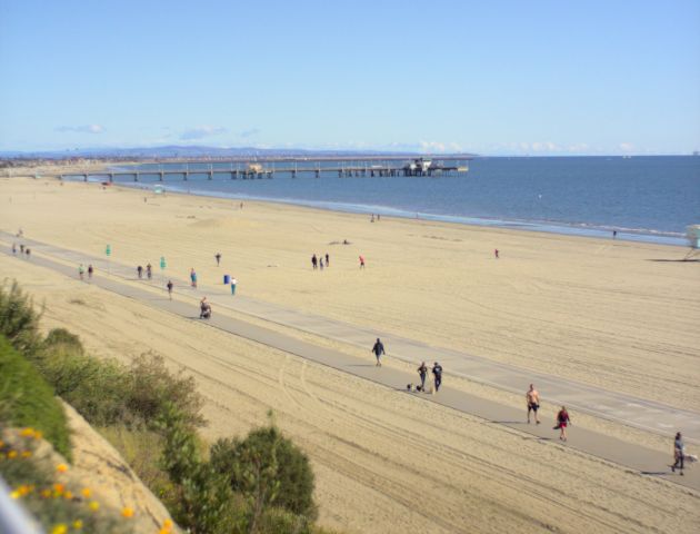 A wide-angle view of a beach with people walking along the shore and a pier in the distance.