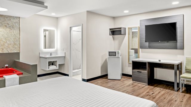 A wide-angle view of a hotel room with a bed, desk, TV, and bathroom.