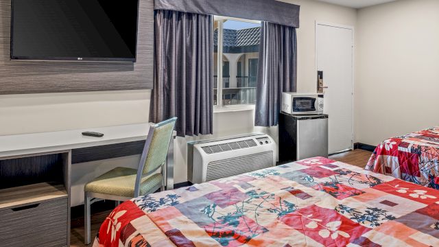 A hotel room with two beds, a desk, a TV, and a window.