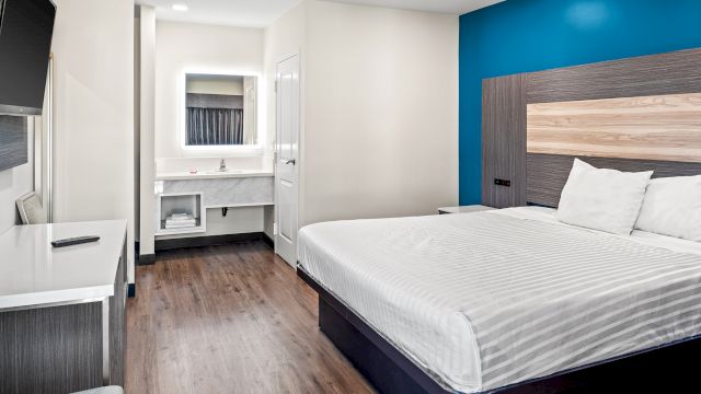 A hotel room with a bed, desk, bathroom, and TV