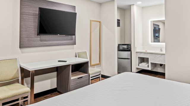 A hotel room with a bed, desk, TV, and mini-fridge.