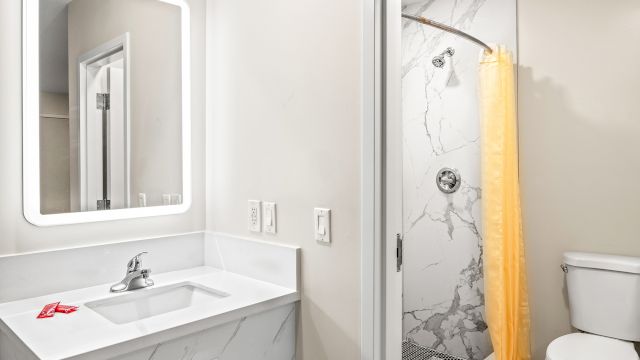 A clean bathroom with a marble shower, toilet, sink, and mirror.