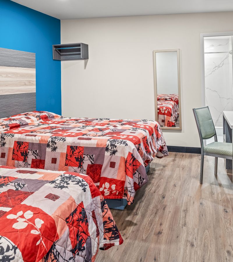 A hotel room with two beds, a mirror, a chair, and a desk.