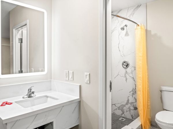 A modern bathroom features a marble sink, illuminated mirror, yellow shower curtain, and toilet within a clean, minimal design.