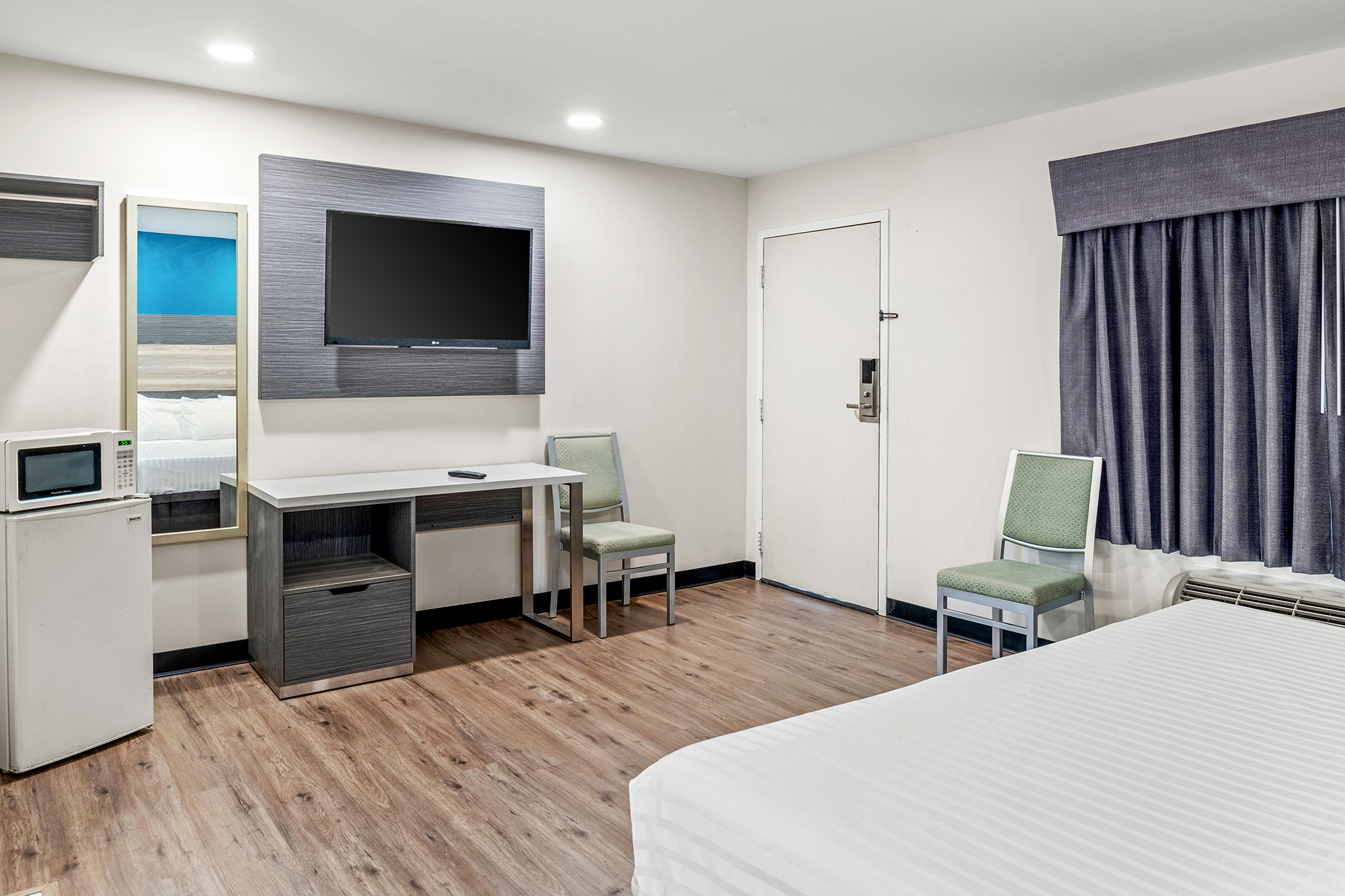 A hotel room with a bed, desk, TV, and refrigerator.
