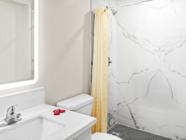 A modern bathroom features a white sink, toilet, marble shower with a yellow curtain, and circular floor tiles.