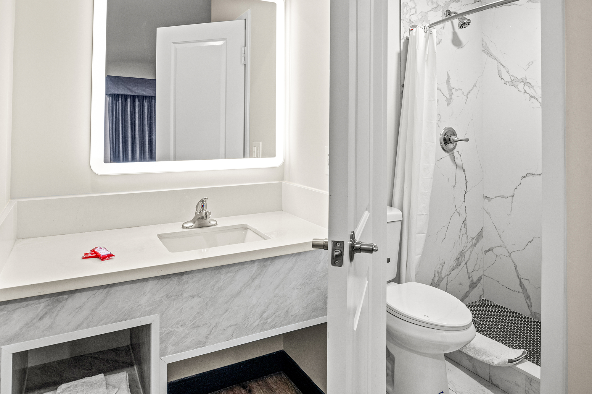 A bathroom with a marble shower, toilet, sink, and mirror.
