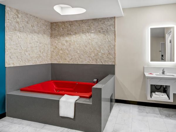 A room with a large red bathtub, tiled walls, a towel, and a modern sink with a mirror.