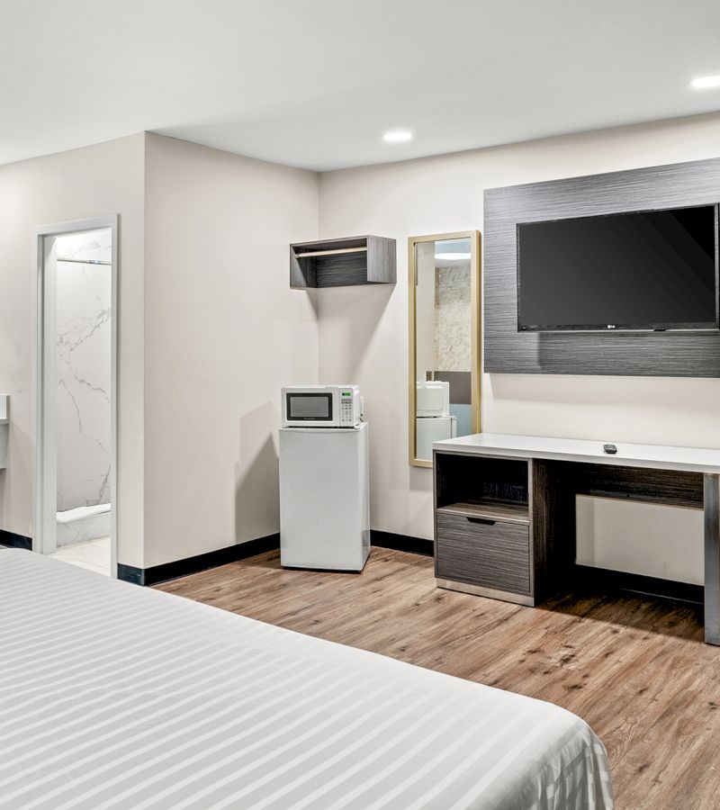 A hotel room with a bed, desk, TV, and mini-fridge
