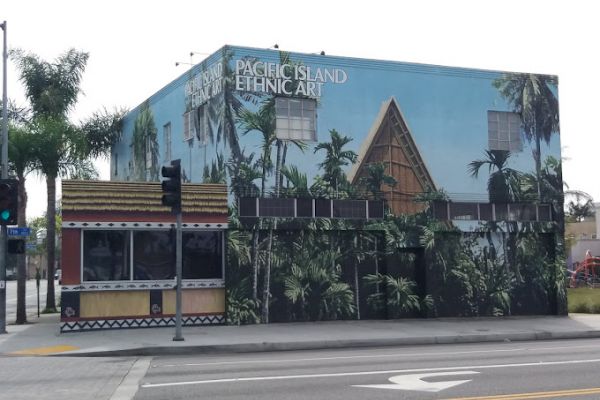 A building features a mural with palm trees and a Pacific island theme, labeled "Pacific Island Ethnic Art," near a street corner.