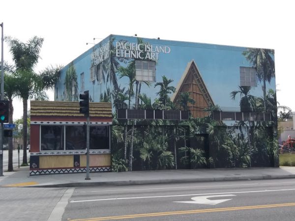 A building features a mural with palm trees and a Pacific island theme, labeled "Pacific Island Ethnic Art," near a street corner.