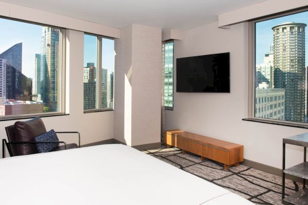 A hotel room with a bed, chair, TV, and city view