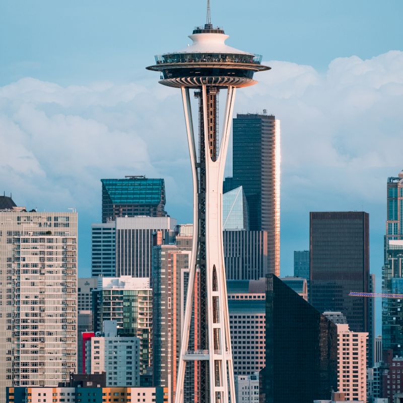 The image shows the Space Needle, a prominent tower amidst the urban skyline of Seattle, with various skyscrapers in the background.