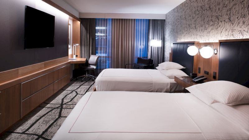 A hotel room with two beds, a desk, and a TV.