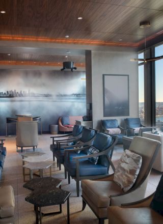 A modern lounge with comfortable seating, large windows offering a scenic view, and a mural of a cityscape on the wall.