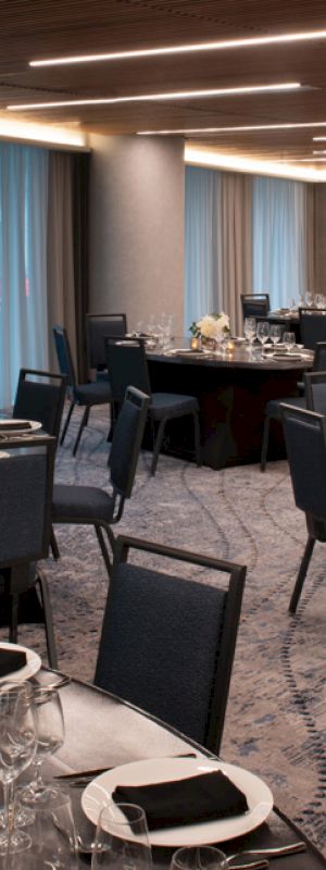 The image shows an elegant banquet room with round tables set for an event, featuring dark chairs and soft lighting.